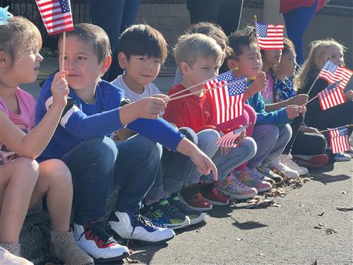 kids sitting on sidewalk waving miniature American flags